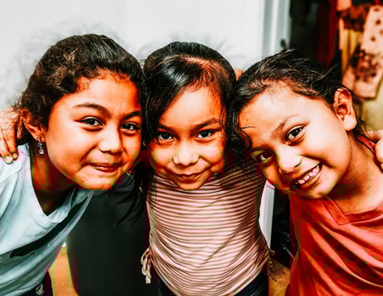 Three young girls with their arms around each other leaning in towards the camera and smiling