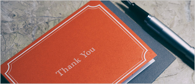 a photo of a thank-you note and pen lying on a marble top table