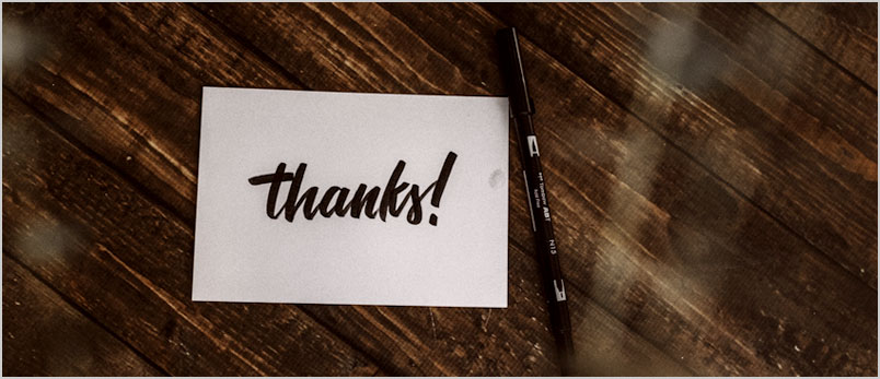 Photo of a thank you note and a pen on a wooden table