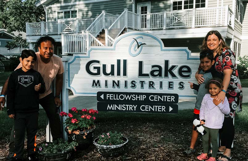 A Gerson, Betsy, and their children standing next to a sign for Gull Lake Ministries
