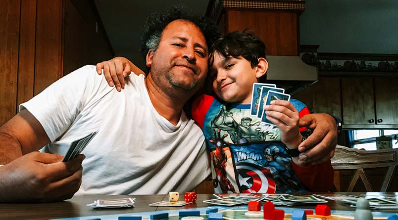 A photo of Gerson with his arm around his younger son while they play a board game
