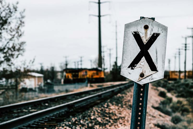 A photo of railroad tracks stretching into the distance with an X on a sign indicating