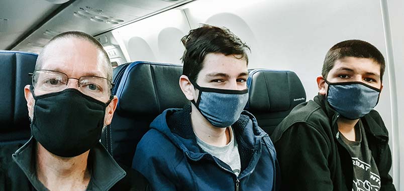 A man and his two teens, wearing masks, sitting on an airplanw
