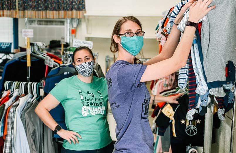 Two women wearing masks hang clothes in a store