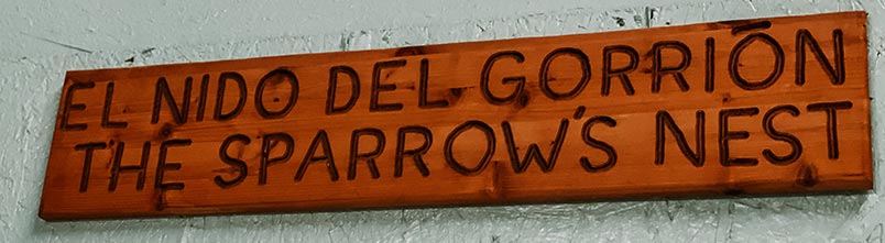 A wooden sign that says The Sparrows Nest in both Spanish and English