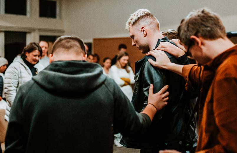 A group of people pray for a young man during a service.