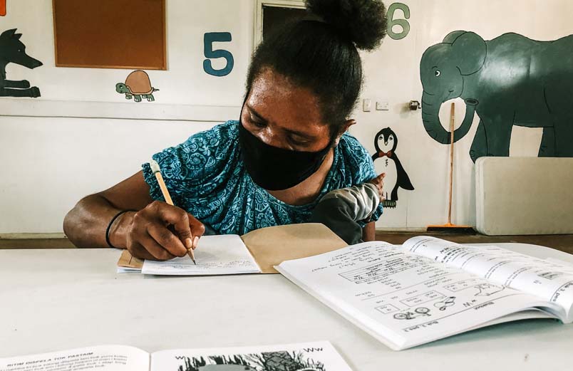 A woman wearing a mask writes in her notebook in a classroom.