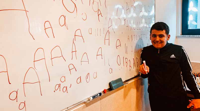 A photo of a student standing at a whiteboard with letters of the alphabet on it.