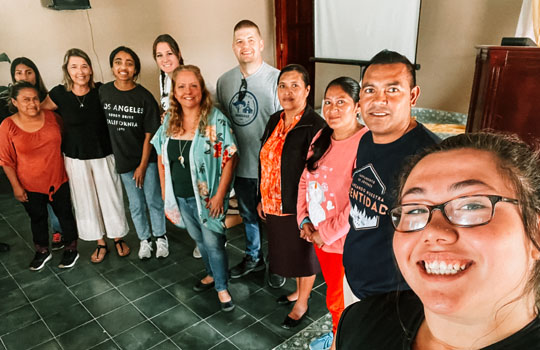 A woman taking a selfie with ten other people in a room