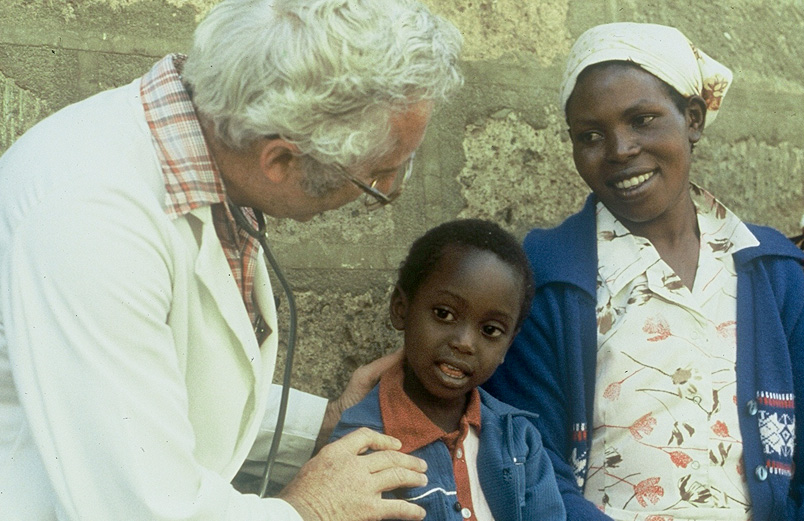 A young boy with his mother, being examined by an older man with a stethescope