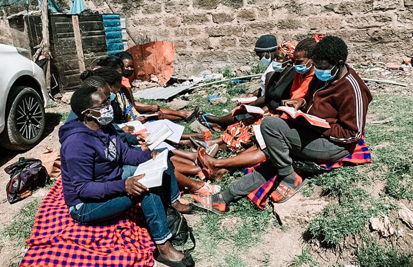 Nine women seated on the ground, studying the Bible together