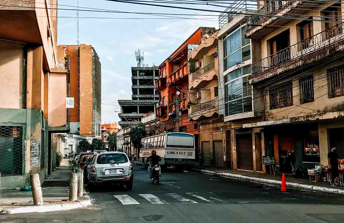 A busy street in Paraguay with cars, a bus, and a person riding a motorcycle