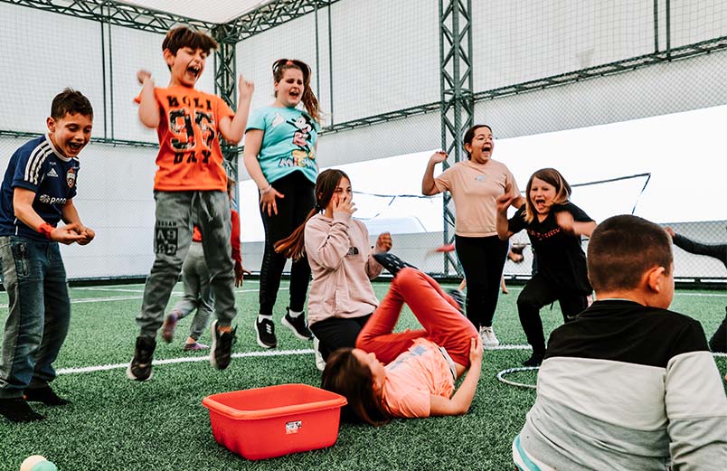 Children jumping up and down and laughing while playing a game inside a soccer complex