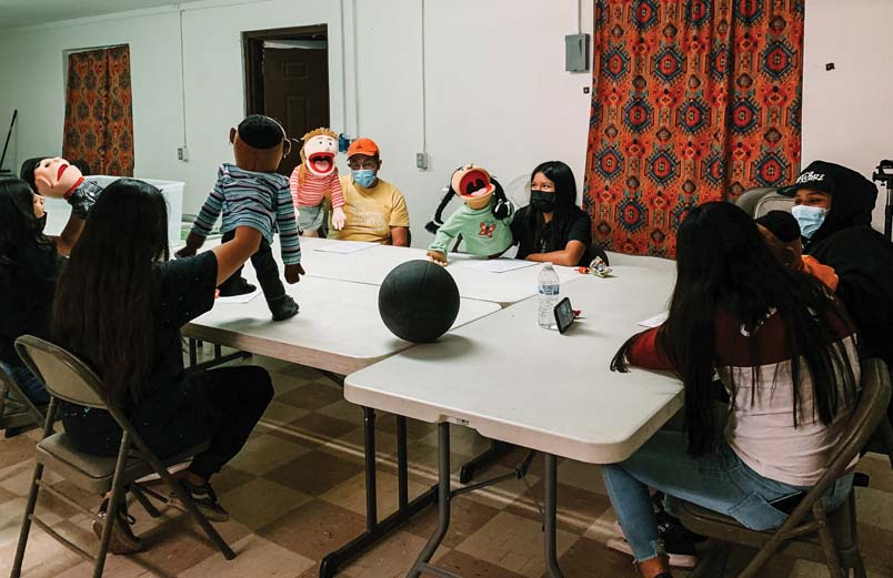Steve Cartwright and a group of youth sitting around a large table practicing with their sock puppets